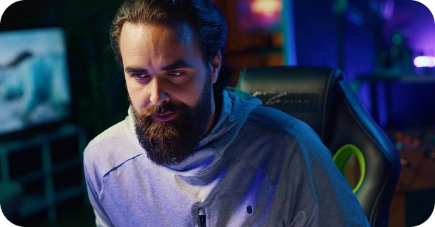 Een geconcentreerde gamer met een baard, die in een gamekamer met RGB-verlichting op een computer speelt, intens gefocust tijdens een online competitieve wedstrijd.